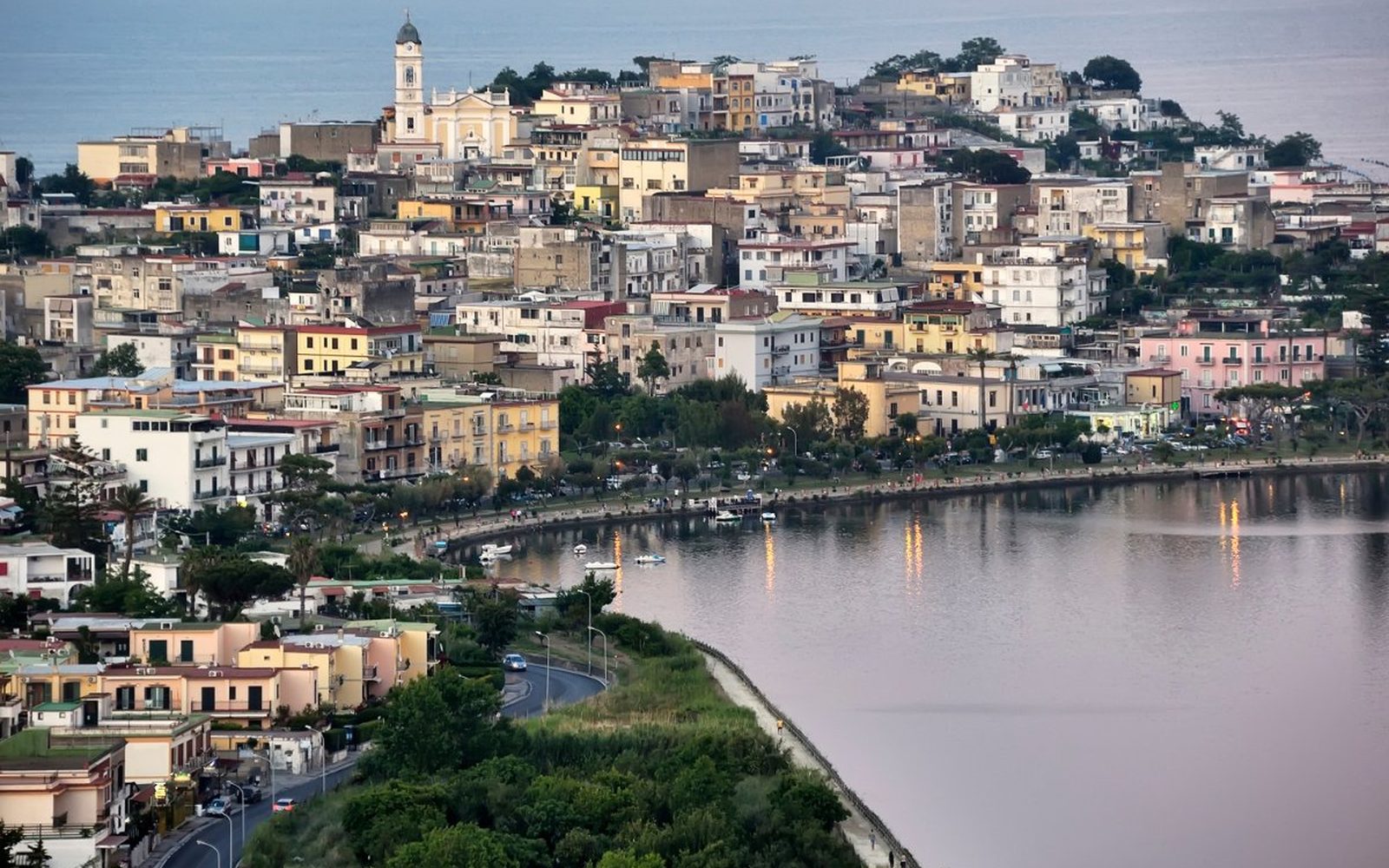 The town of Bacoli on the bay at dusk, lights reflecting on the still water of the Phlegraean coast