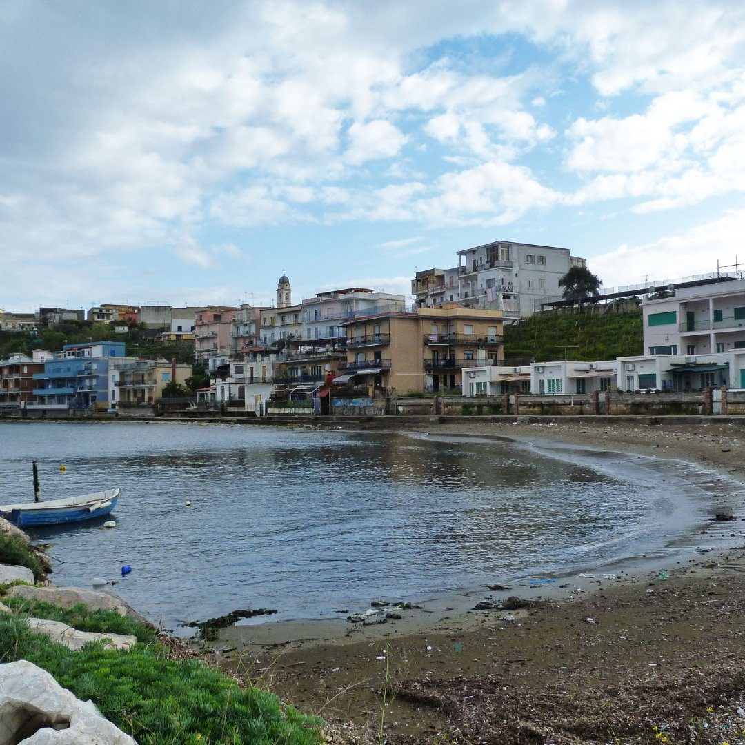 The pastel houses and small curving beach of the fishing village of Bacoli with a moored blue boat in the foreground