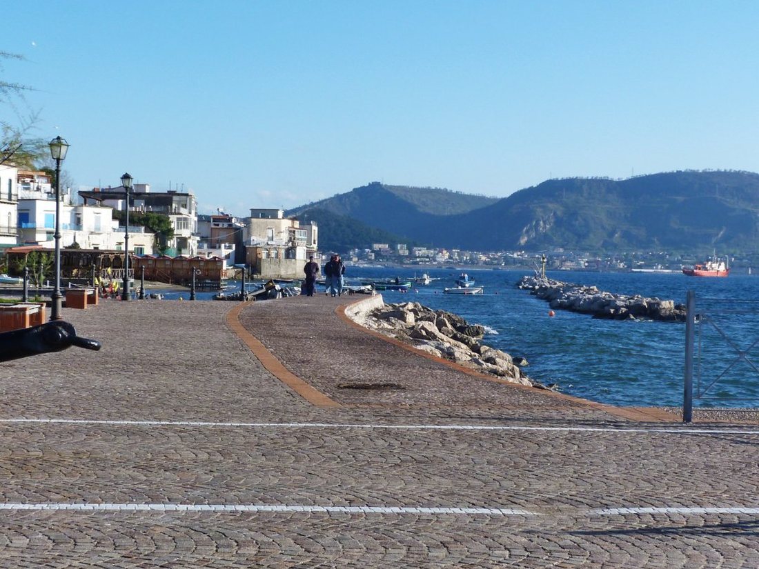 The cobbled seafront promenade of Bacoli on the Bay of Pozzuoli, with fishing boats and the volcanic headlands beyond