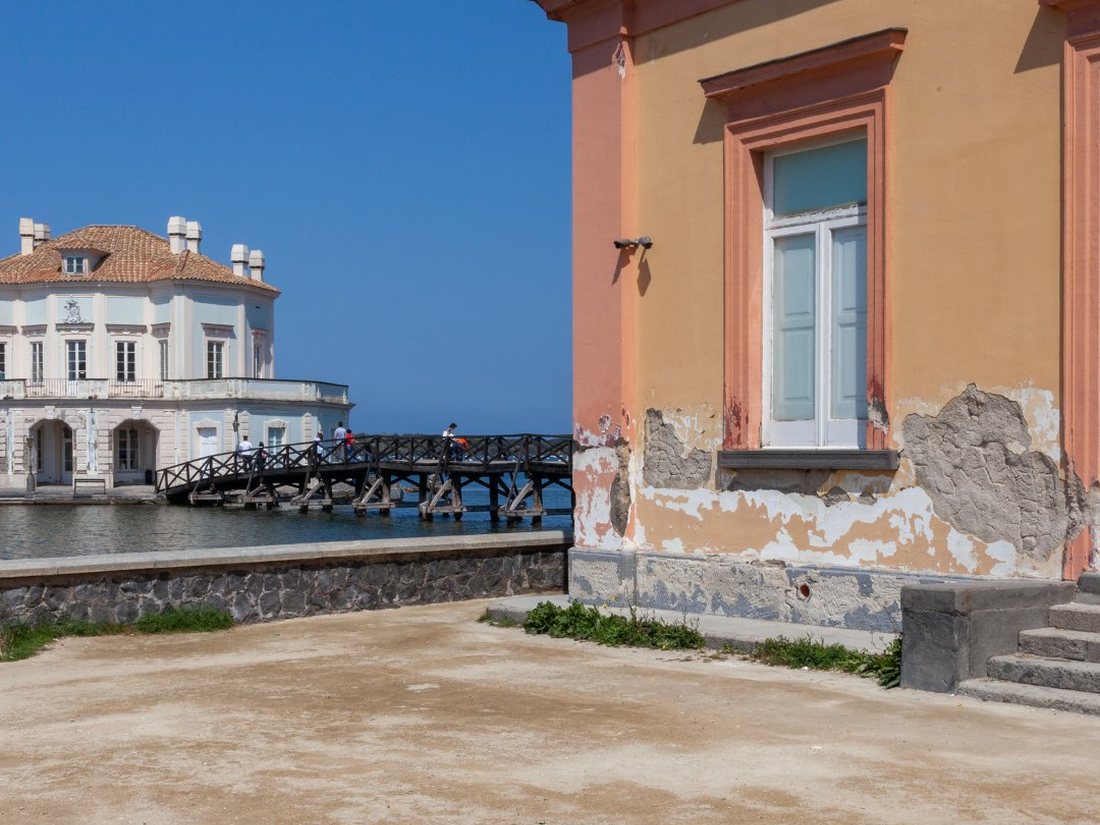 The Casina Vanvitelliana pavilion seen across Lake Fusaro at Bacoli beside a weathered Bourbon-era building