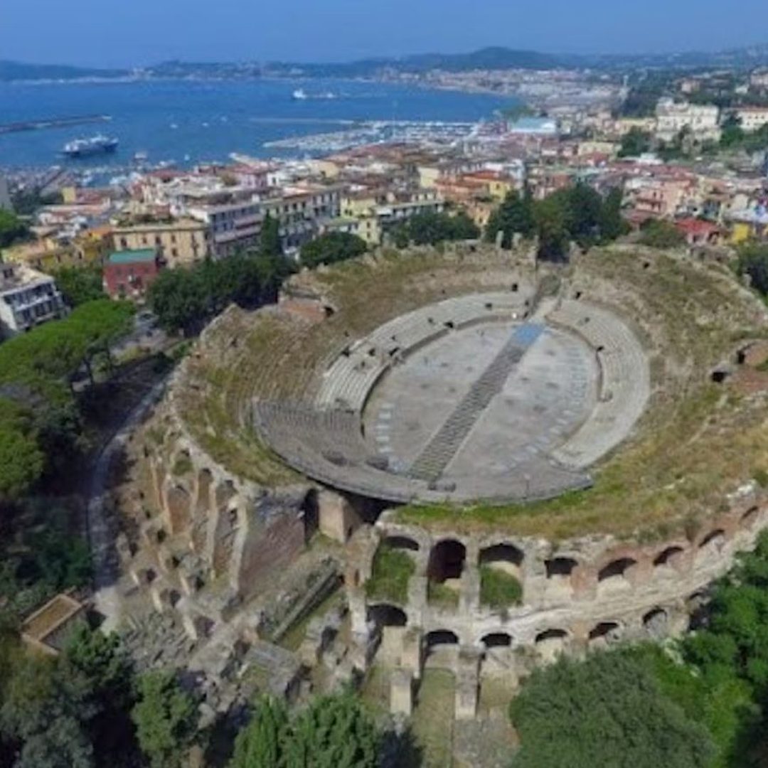 Aerial view of the oval Flavian Amphitheater of Pozzuoli set within the town, with the Bay of Pozzuoli behind
