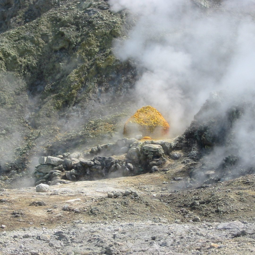 Close-up of a Solfatara fumarole — bright yellow sulfur crystals around a vent releasing dense white volcanic steam