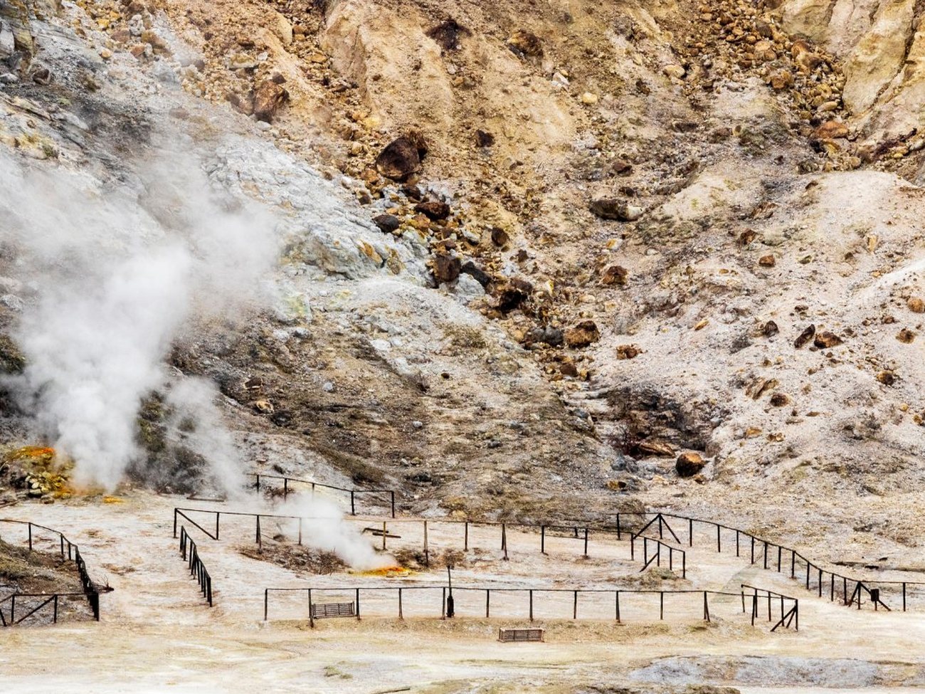 The Solfatara crater at Pozzuoli — white steam rising from fumaroles across a pale, sulfur-streaked volcanic floor ringed by safety railings