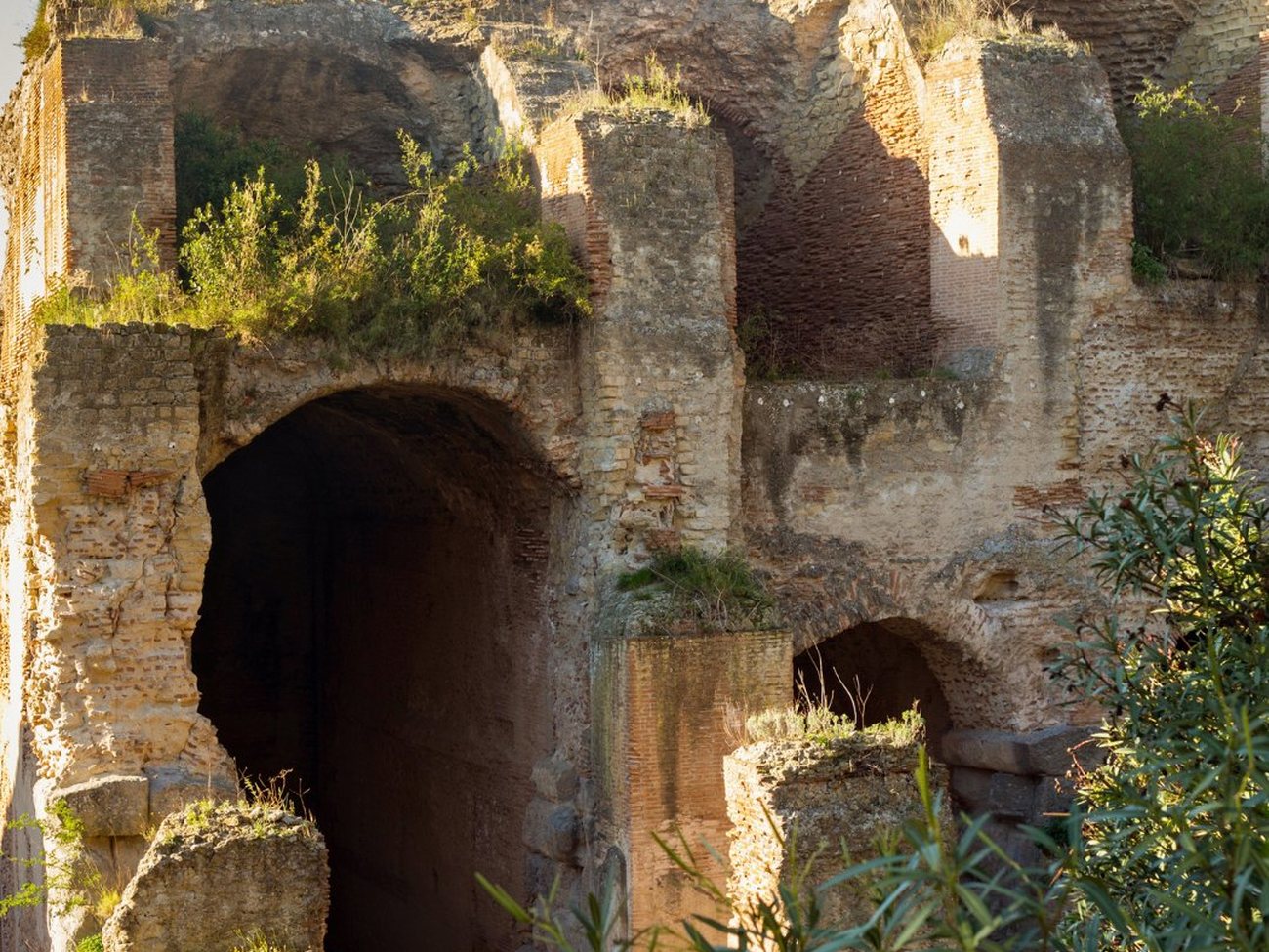 The archaeological park of the Terme di Baia at sunset — towering brick walls and arches of the Roman imperial thermal complex above the bay